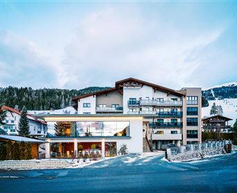 Ein modernes Hotel in einer winterlichen Landschaft mit schneebedeckten Bergen. Die Fassade besteht aus einer Kombination von Holz und Glas.