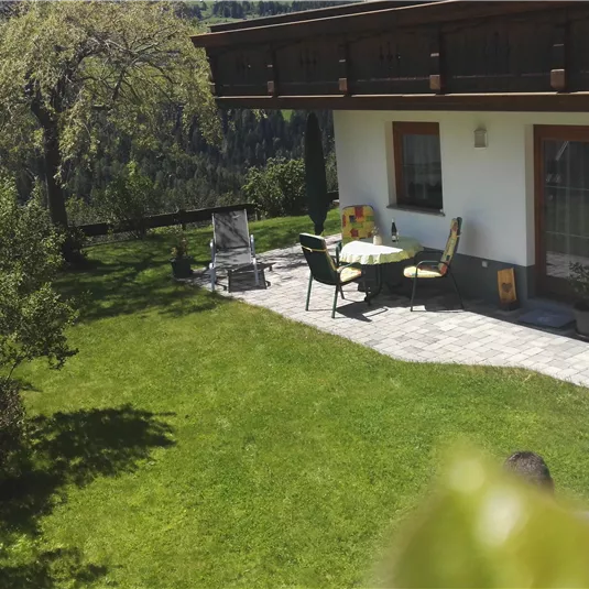 A green meadow with a cozy seating area in front of a house. The garden is surrounded by trees and offers a quiet, idyllic atmosphere.