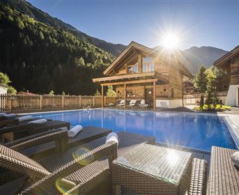 Ein modernes Ferienhaus mit einem Pool im Vordergrund. Die sonnige Berglandschaft rundet die entspannende Atmosphäre ab.