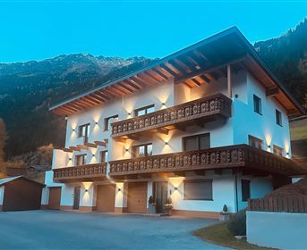 A modern house with several balconies and beautiful wood decor. In the background, mountains and a blue sky can be seen.