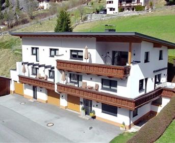 A modern house with several balconies in an idyllic setting. In the background, green hills and residential houses are visible.