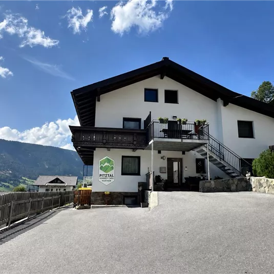 A modern house with a spacious terrace and a clear sky in the background. The surrounding landscape is characterized by mountains and greenery.