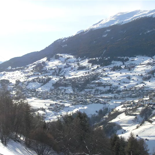 A snowy mountain landscape with a picturesque valley. In the background, the snow-capped peaks are visible.
