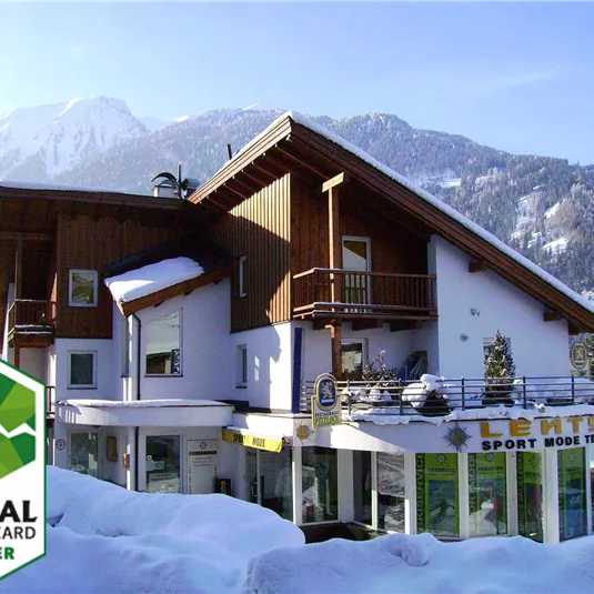A cozy building in the snow with a mountain landscape in the background. It features a sports shop and is a partner of the Pitztal Summer Card.