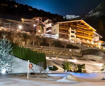 A wintry terrain with snow-covered areas and illuminated buildings. The night sky shines brightly over a cozy mountain landscape.