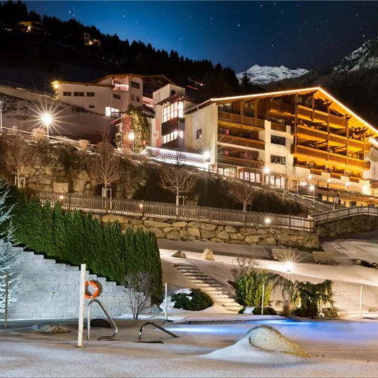 A wintry terrain with snow-covered areas and illuminated buildings. The night sky shines brightly over a cozy mountain landscape.