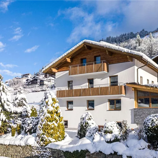 A beautiful, modern house in a snow-covered landscape.
Surrounded by snow-covered trees and mountains under clear sky.