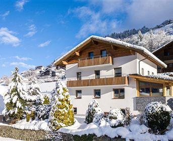 Ein wunderschönes, modernes Haus in einer schneebedeckten Landschaft. Umgeben von schneebedeckten Bäumen und Bergen unter klarem Himmel.