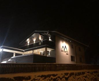 A modern building with a illuminated facade in a wintery environment. It is night, and the lights give the house an inviting charm.