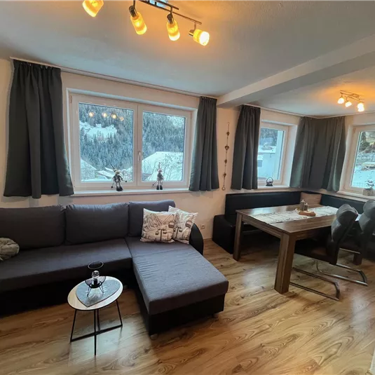 A cozy living room with a modern couch and a dining area. Large windows provide a view of the snowy landscape.