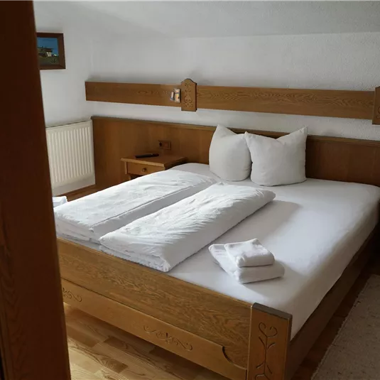 Ein einfaches, gemütliches Schlafzimmer mit einem großen Bett und Holzdetails. Zwei Kopfkissen und frische Handtücher liegen bereit.