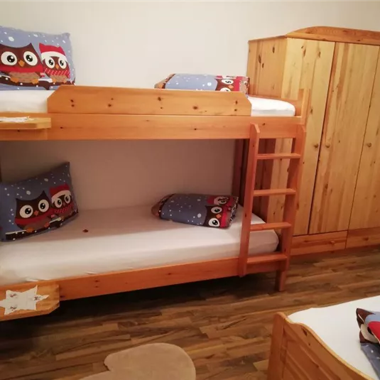 Ein gemütliches Kinderzimmer mit einem Etagenbett aus Holz. Auf den Kissen sind Eulenmotiven und ein Kleiderschrank aus Holz steht ebenfalls im Raum.