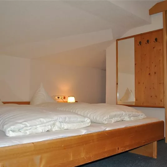 A cozy bedroom with a double bed and two pillows. In the background, you can see a mirror and a bathroom with a sink.