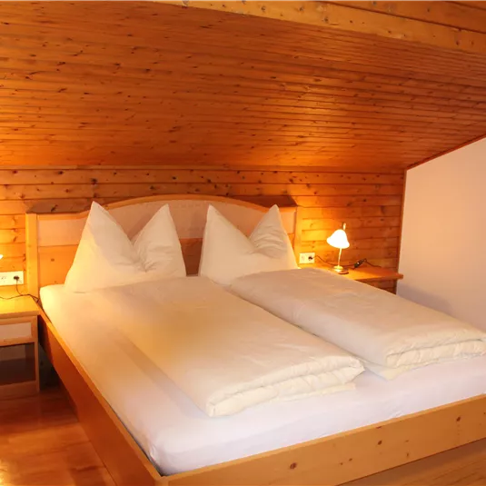 A cozy bedroom with a double bed and wooden paneling. Soft lighting creates a warm atmosphere.